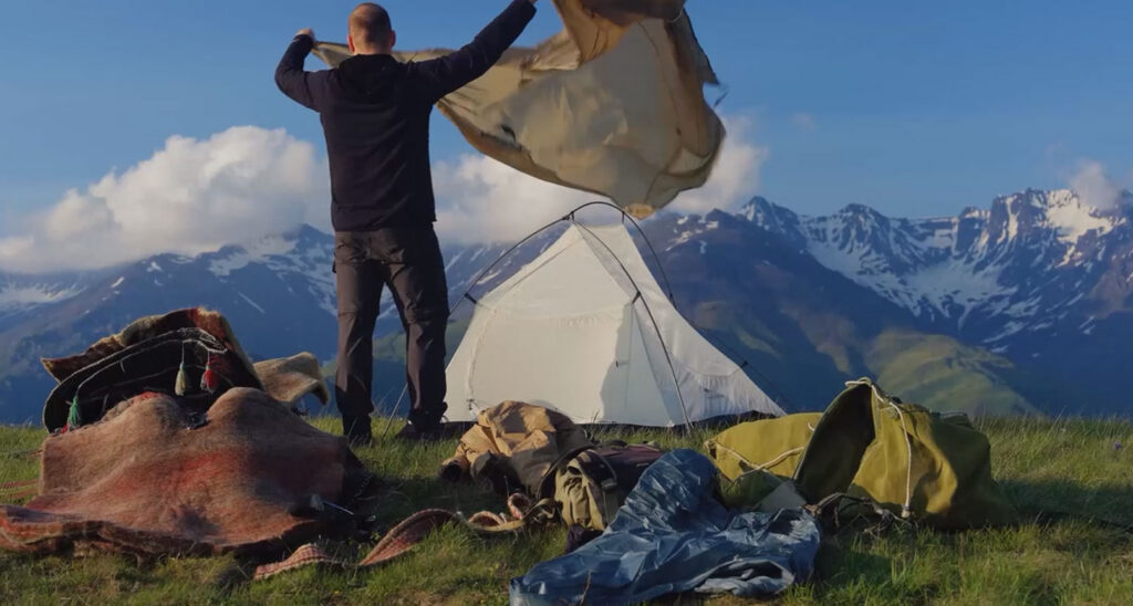 Zeltlager auf einer Bergwiese im Großen Kaukasus, dahinter schneebedeckte Gipfel